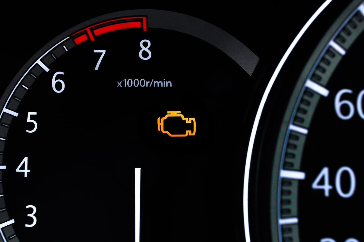 Closeup of a car dashboard with an illuminated check engine light and the tachometer displaying engine revolutions per minute